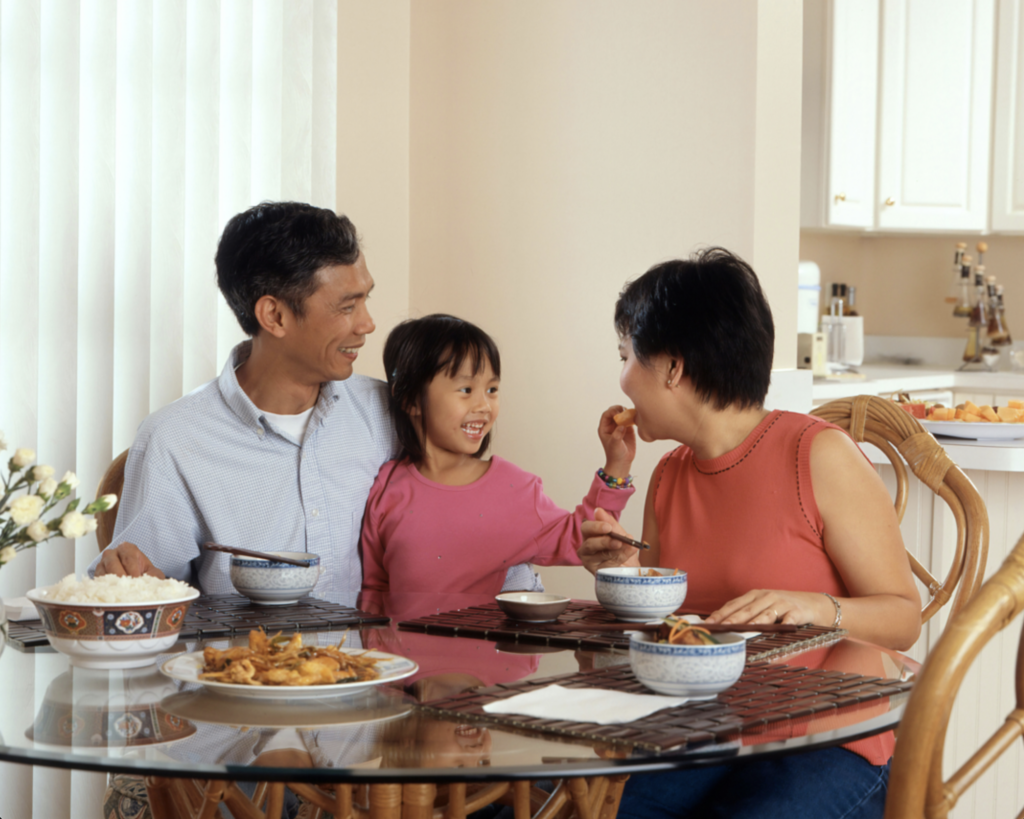 An Asian nanny enjoys a meal at a kitchen table with her family.